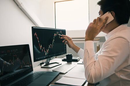 Agent trader man talking at telephone and checking business stock data on computer in office room.の写真素材