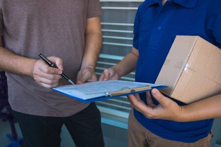 Delivery young man standing at the door of home and carrying parcels for young male to signing.