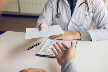 Asian male doctor talking in clinic room and handing a prescription to the patient.の写真素材