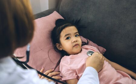 Asian little girl a woman slept in a pillow on the sofa for a female doctor using stethoscope on a heartbeat at home.の写真素材