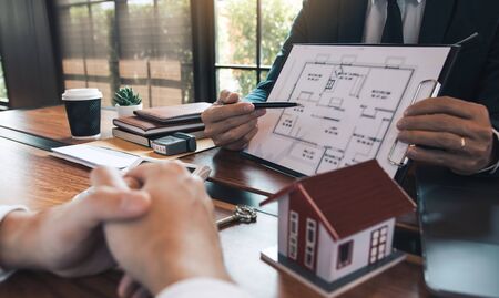 Agents are using pens pointing to blueprint home design and are being explained to customers at the...