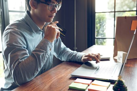 Online shopping concept with man hand using laptop and looking credit card for purchase order...