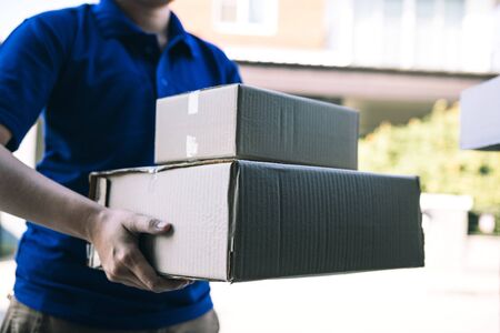 Asian cargo carrier holds a cardboard box with the package inside and the recipient is signing the...