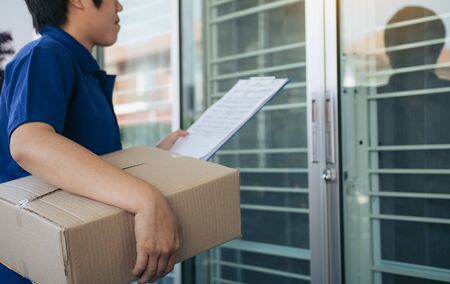 Asian cargo carrier holds a cardboard box with the package inside and the recipient is signing the...