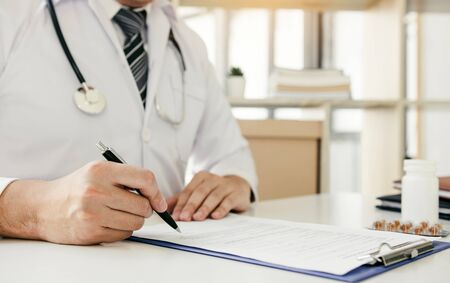 Doctor hand holding pen writing patient history list on note pad and talking to the patient about medication and treatment.の写真素材