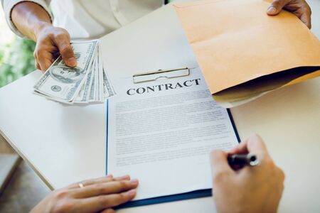 Money in the hands of businessmen who are submitting to entrepreneurs to force the signing of contract documents about corruption concept.の写真素材