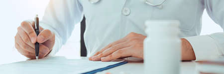 Doctor hand holding pen writing patient history list on note pad and talking to the patient about medication and treatment.の写真素材