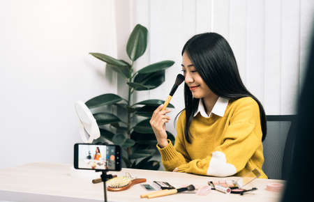 Beautiful asian woman blogger using camera phone recording vlog video live streaming and showing how to make up cosmetics at home.の写真素材