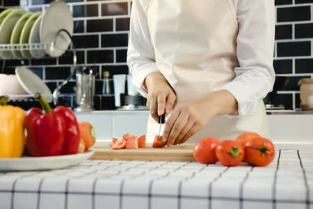 Housewife using knife and hands cutting tomato on wooden board in kitchen room.