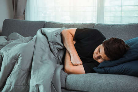Asian man feel the illness while he was cold lying on the sofa and wearing a blanket at his house.の写真素材
