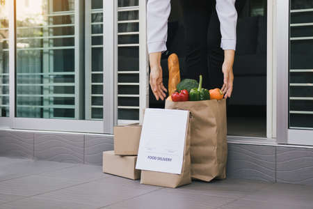 Asian woman open the door and took the bag of food ordered by the carrier to put in front of the house to prevent the epidemic.の写真素材