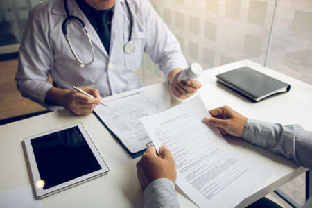 Confident doctor man holding a pill bottle and talking with senior patient and reviewing his medication at office room.の写真素材