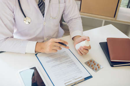 Confident doctor man holding a pill bottle and writing while talking with senior patient and...