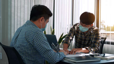 Asian colleagues are working in the office while wearing masks during the outbreak of the virus.