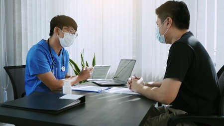Doctors are explaining the treatment of a sick patient in tablets while wearing a mask during the virus outbreak.の写真素材