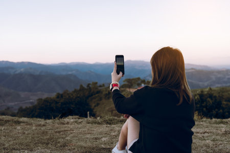 Asian female tourists use their mobile phones to take pictures of the scenery at the top of a fresh mountain hill.の写真素材