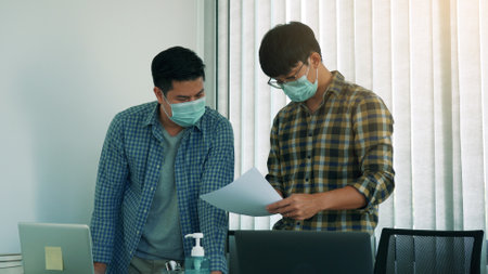 Asian colleague stood at the office and analyzed corporate data while wearing a face maskの写真素材