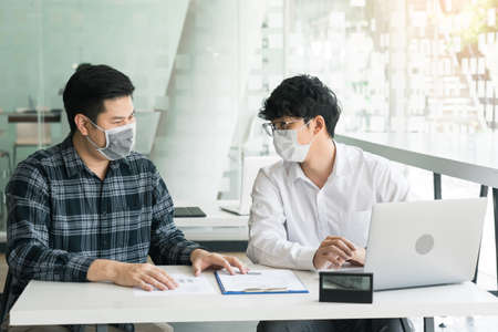 Asian colleague works while wearing a mask in the office during COVID-19.の写真素材