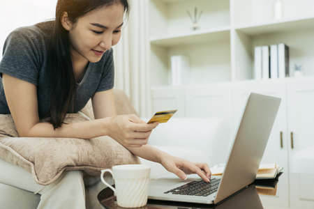 Asian woman holding a credit card for online shopping while sitting on the couch while on vacation...
