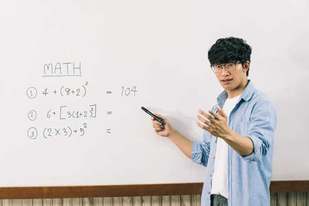 Asian male teacher is teaching students at the classroom while pointing at numbers on the white...