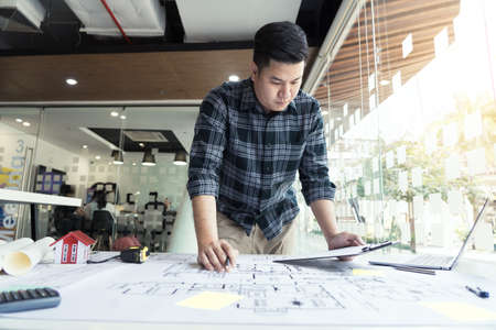 Interior designer or architect reviewing blueprints and holding pencil drawing on desk at home office.の写真素材