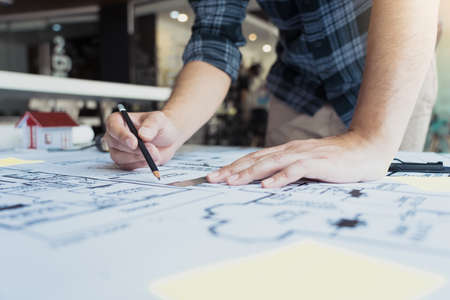 Interior designer or architect reviewing blueprints and holding pencil drawing on desk at home office.の写真素材
