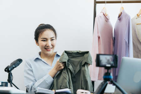 Young asian entrepreneurs are picking up their clothes to show off to customers through online sales on a live phone.の写真素材