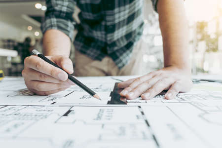 Interior designer or architect reviewing blueprints and holding pencil drawing on desk at home...