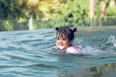 Little asian boy plays in the water while swimming in the pool wearing armbands.の写真素材