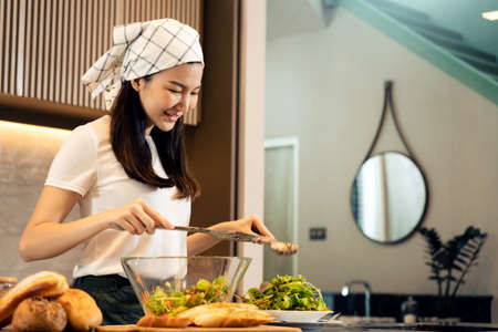 Asian housewife preparing fresh vegetables to make salad at home kitchen counter.の写真素材