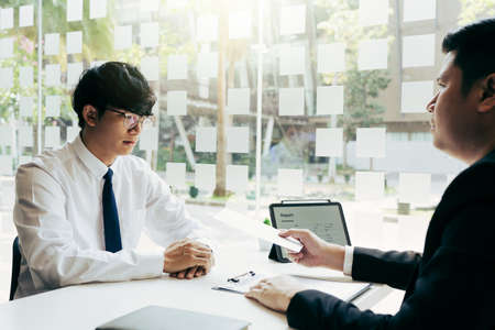 Male manager is talking or explaining about having to dismiss the employee while being handed out a resignation envelope to the employee.の写真素材