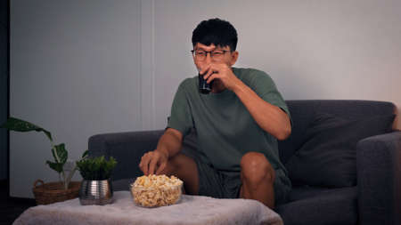 Asian guy is relaxing for the weekend by watching series his home at night.