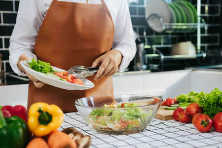 Asian woman is pouring ingredients that are prepared to make a salad into a salad bowl.の写真素材
