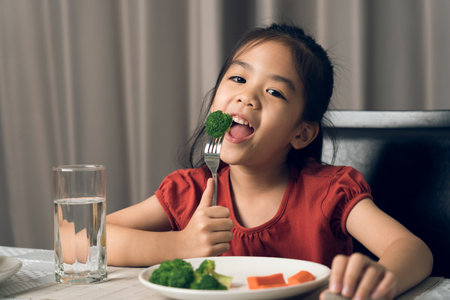 Asian little girl eating healthy vegetables with relish.の写真素材