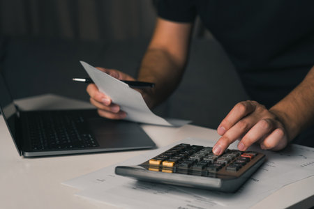 Asian man using calculator to calculate expenses while holding family bills at his home.の写真素材