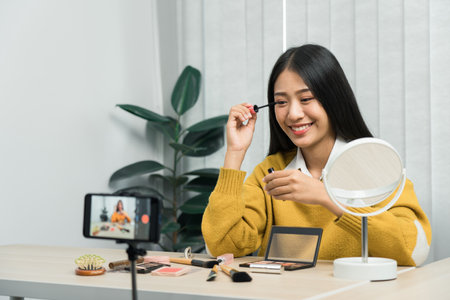 Beautiful asian woman blogger using camera phone recording vlog video live streaming and showing how to make up cosmetics at home.の写真素材