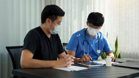 Doctors are explaining the treatment of a sick patient in tablets while wearing a mask during the virus outbreak.の写真素材
