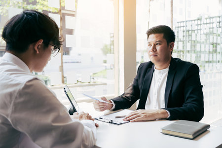 Male manager is talking or explaining about having to dismiss the employee while being handed out a resignation envelope to the employee.の写真素材