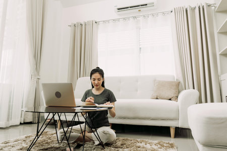 Young asian woman sits in the living room using a calculator to calculate family income and expenses...