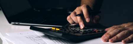 Asian man is using a calculator to calculate his family's monthly miscellaneous expenses at his home.の写真素材