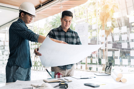 Architects or engineering working with blueprints and discussing project together at the meeting in the office.の写真素材