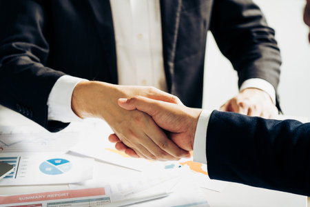 Entrepreneurs collaboration deal shaking hands in a modern office and financial paper graph on desk.の写真素材