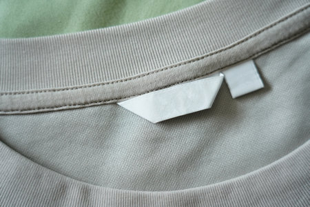 Close up of blank white clothing care label on shirt fabric background.