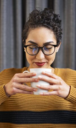 A woman wearing glasses smells her coffee and smilesの写真素材