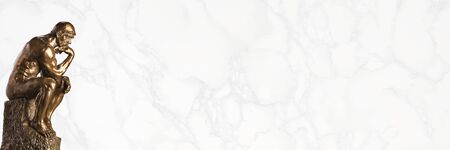 A bronze replica statue of Rodin's Thinker on a white marble background