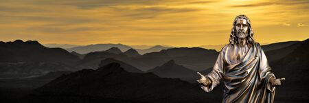 A bronze statue of a Jesus Christ with a sunset background with jagged hillsの写真素材