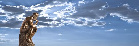 A bronze replica statue of Rodin s Thinker on a dramatic cloudy sky backgroundの写真素材