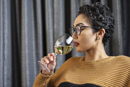 A woman wearing glasses and a sweater drinking white wineの写真素材
