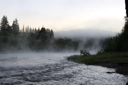 a stormy taiga river, surrounded by rocky banks, in the early morning, wrapped in thick fogs.の写真素材