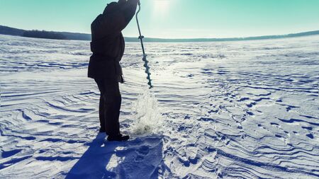 Fisherman drills the ice. Winter fishing.の写真素材